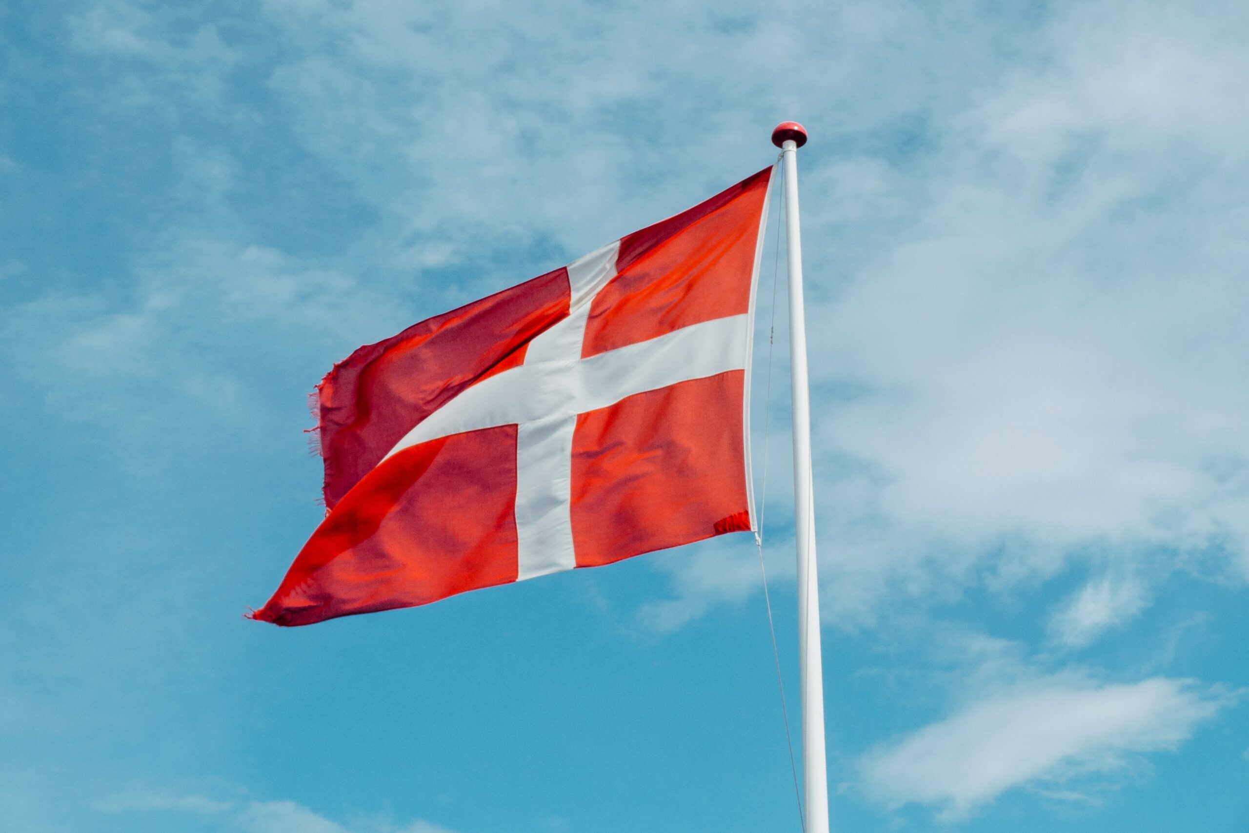 Die dänische Flagge weht an einer Fahnenstange vor blauem Himmel mit weißen Wolken.